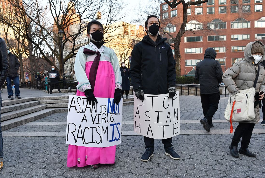A woman wearing a Korean hanbok holds a sign that says "Asian is not a virus, racism is" while a man holds a sign that says "Stop Asian hate"